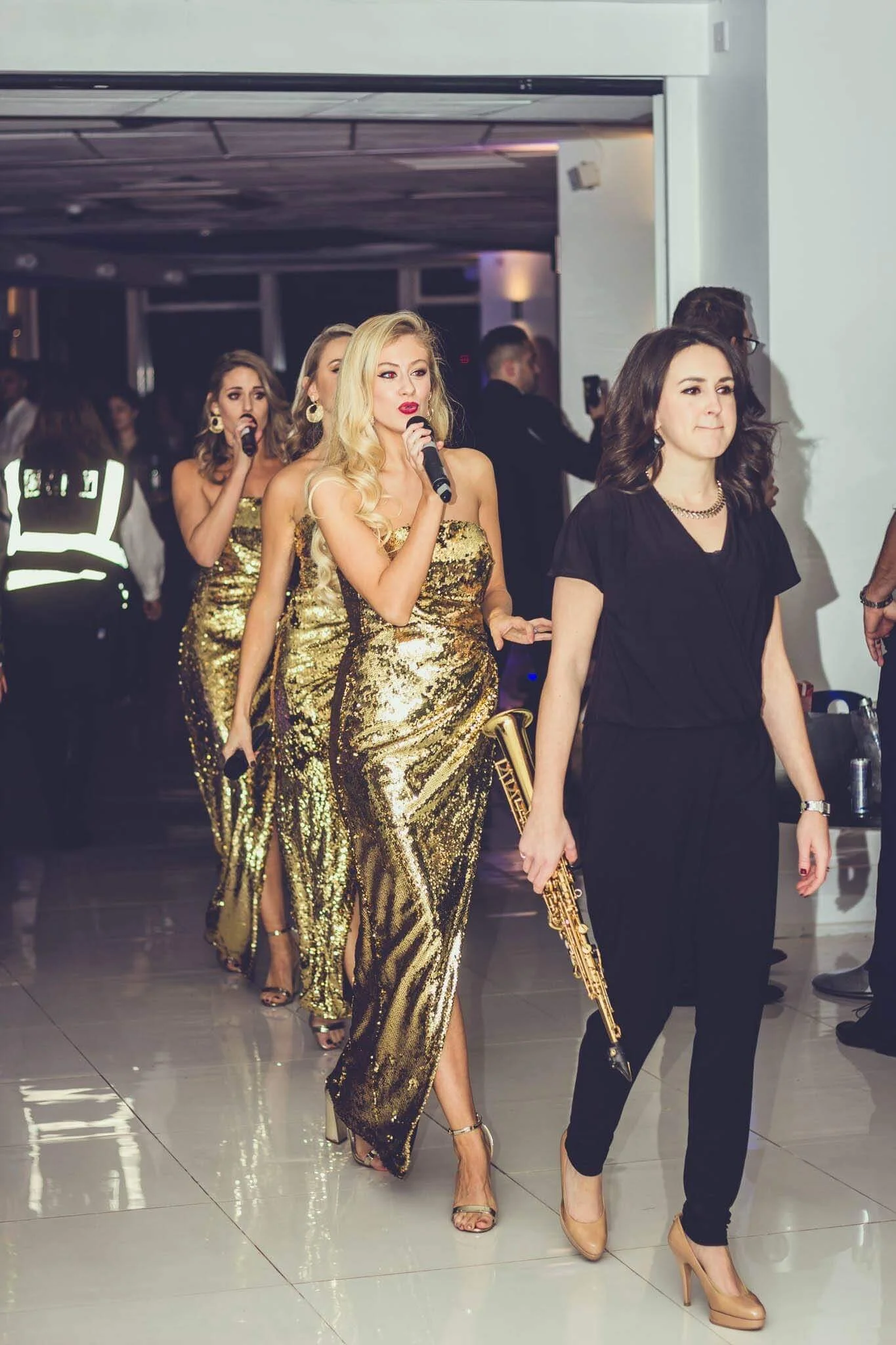 The Roxys in gold gowns, entering a London event with a live saxophonist
