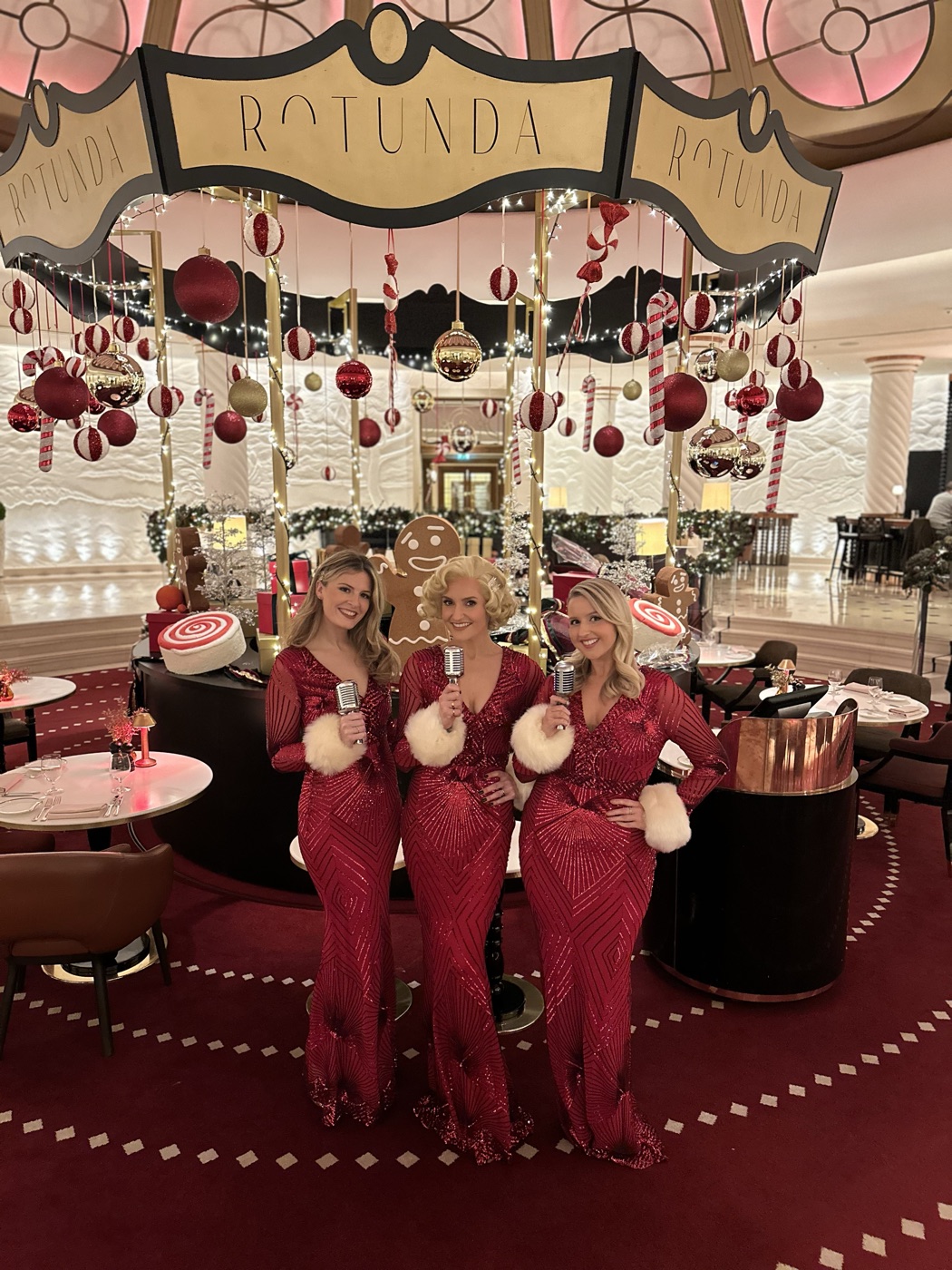 The Roxys, a London vocal jazz trio in red sequin gowns with vintage microphones, at a luxury London hotel dressed for Christmas